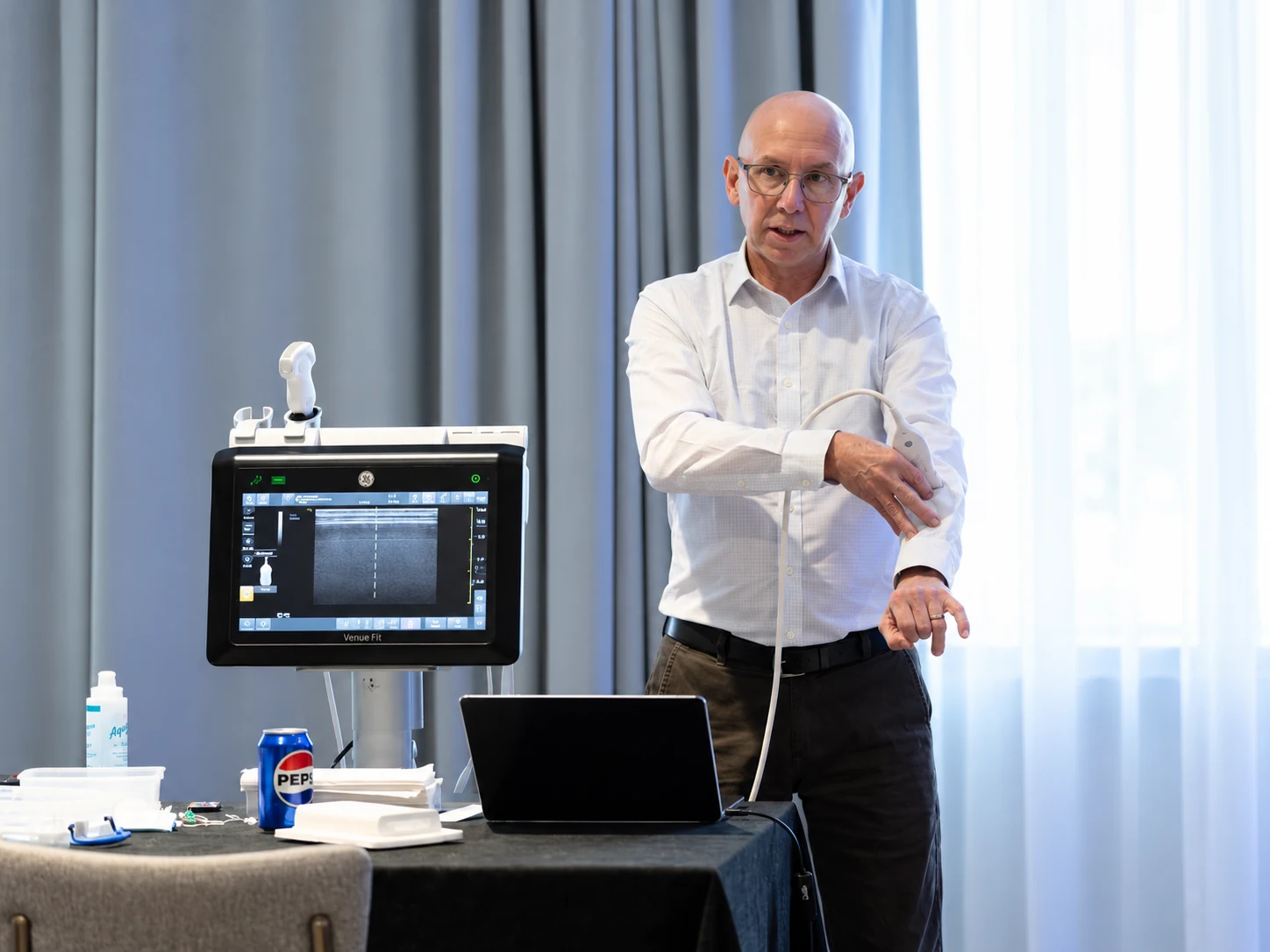 An educator demonstrates ultrasound probe handling beside a portable ultrasound system.